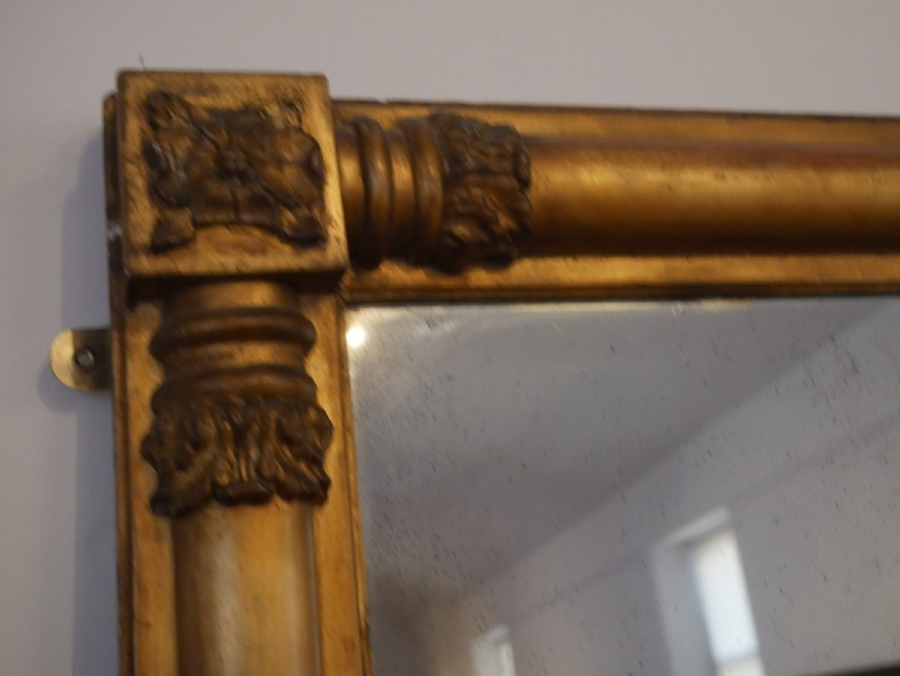 A broad rectangular late Regency giltwood overmantel mirror featuring a reeded frame with carved corner rosettes and central moulding accents. View III