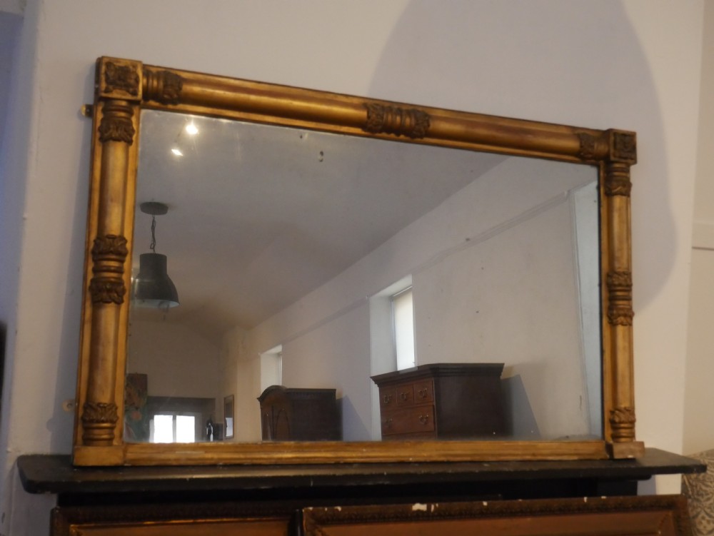 A broad rectangular late Regency giltwood overmantel mirror featuring a reeded frame with carved corner rosettes and central moulding accents. View X