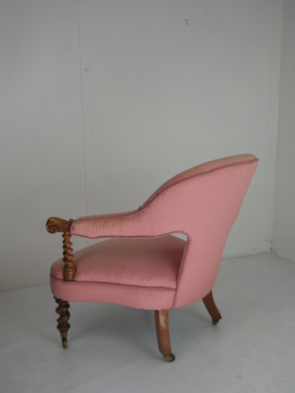 A Victorian armchair upholstered in dusty pink patterned fabric featuring carved walnut barley-twist legs and arm supports set on brass castors. View X