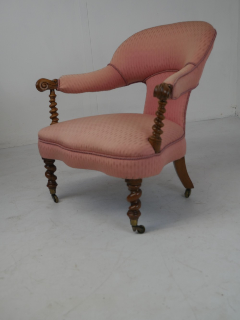 A Victorian armchair upholstered in dusty pink patterned fabric featuring carved walnut barley-twist legs and arm supports set on brass castors. View XII