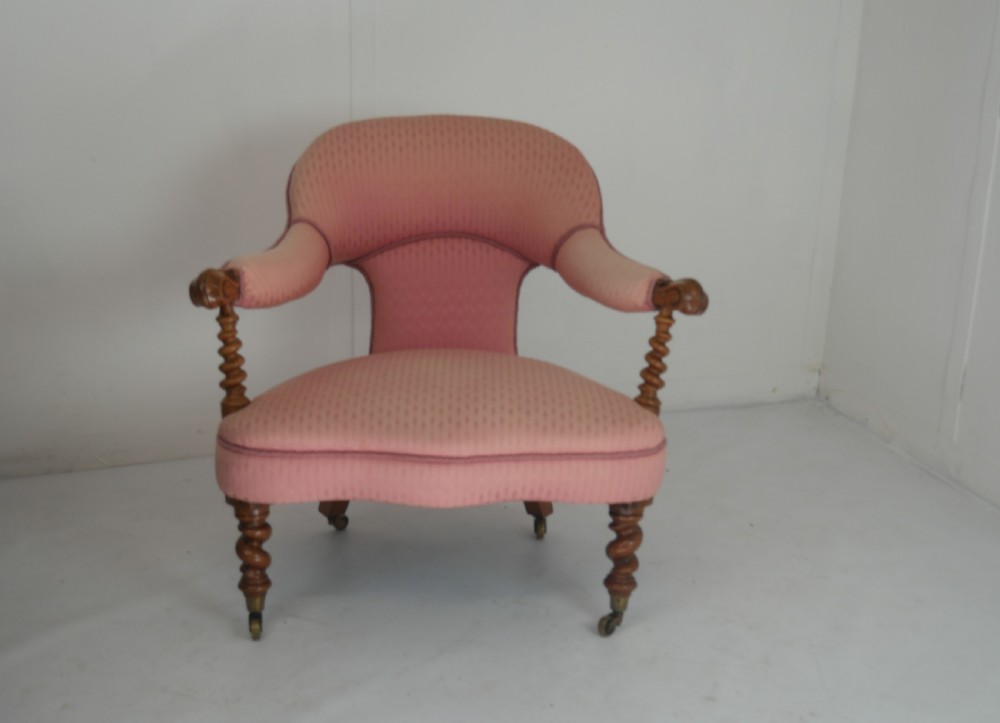 A Victorian armchair upholstered in dusty pink patterned fabric featuring carved walnut barley-twist legs and arm supports set on brass castors.