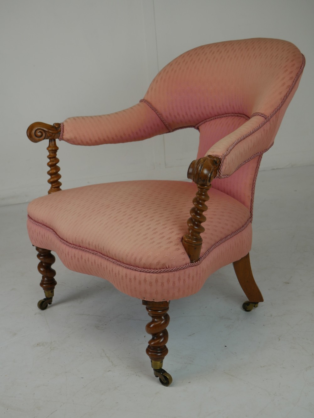 A Victorian armchair upholstered in dusty pink patterned fabric featuring carved walnut barley-twist legs and arm supports set on brass castors. View II