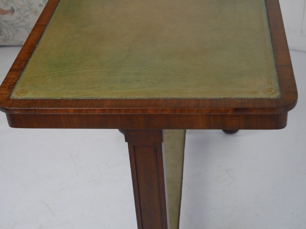 A 19th-century mahogany side table featuring an inset olive green leather top, supported by a trestle base with carved scroll feet. View V