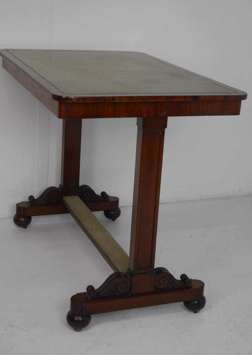A 19th-century mahogany side table featuring an inset olive green leather top, supported by a trestle base with carved scroll feet. View IX