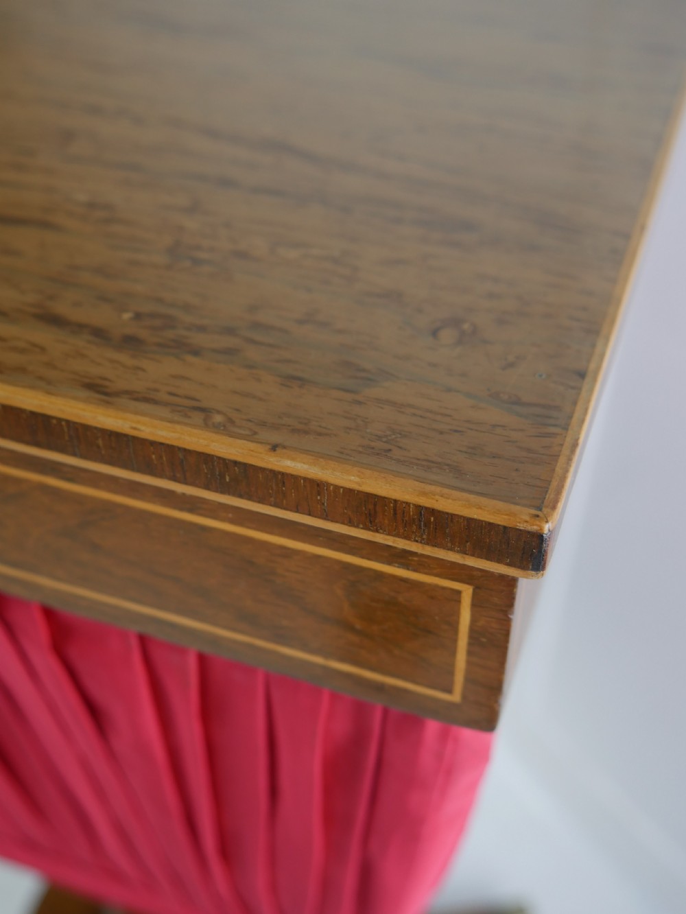 A Regency mahogany sewing table featuring a rectangular top with string inlay, a pleated red fabric work bin below, a turned pedestal support, and four splayed legs with brass castors. View III