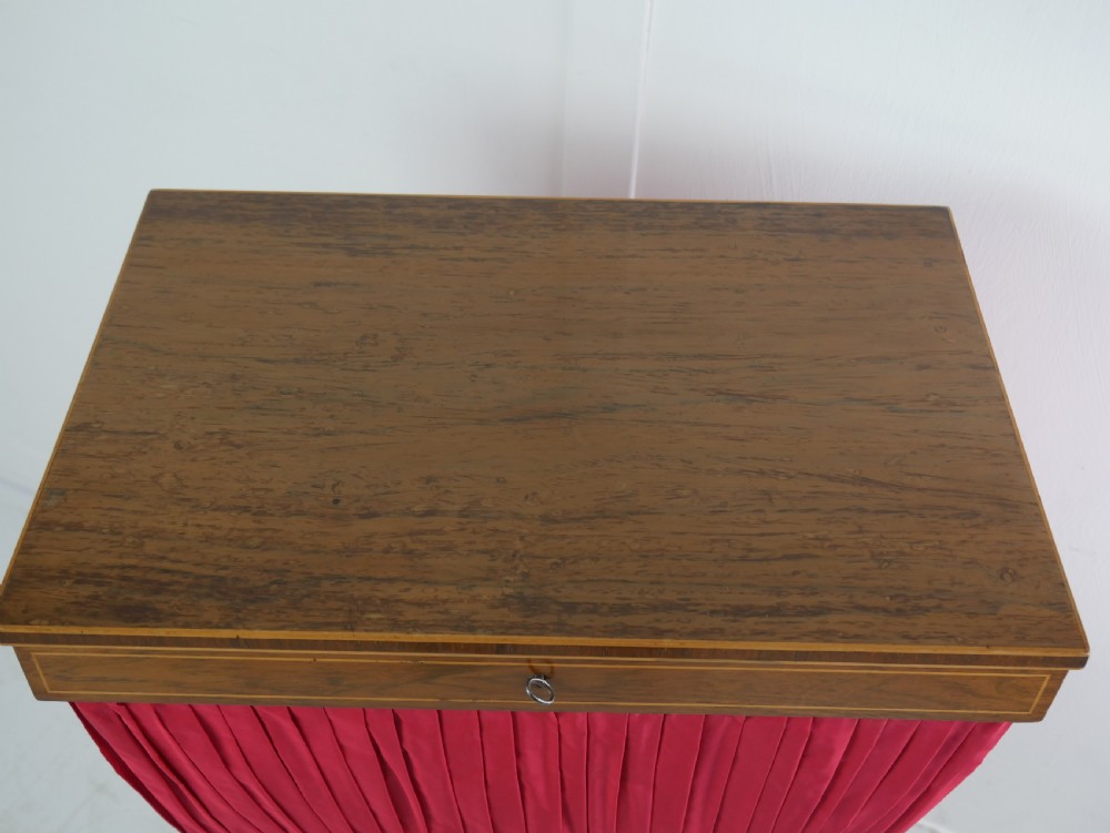 A Regency mahogany sewing table featuring a rectangular top with string inlay, a pleated red fabric work bin below, a turned pedestal support, and four splayed legs with brass castors. View IV