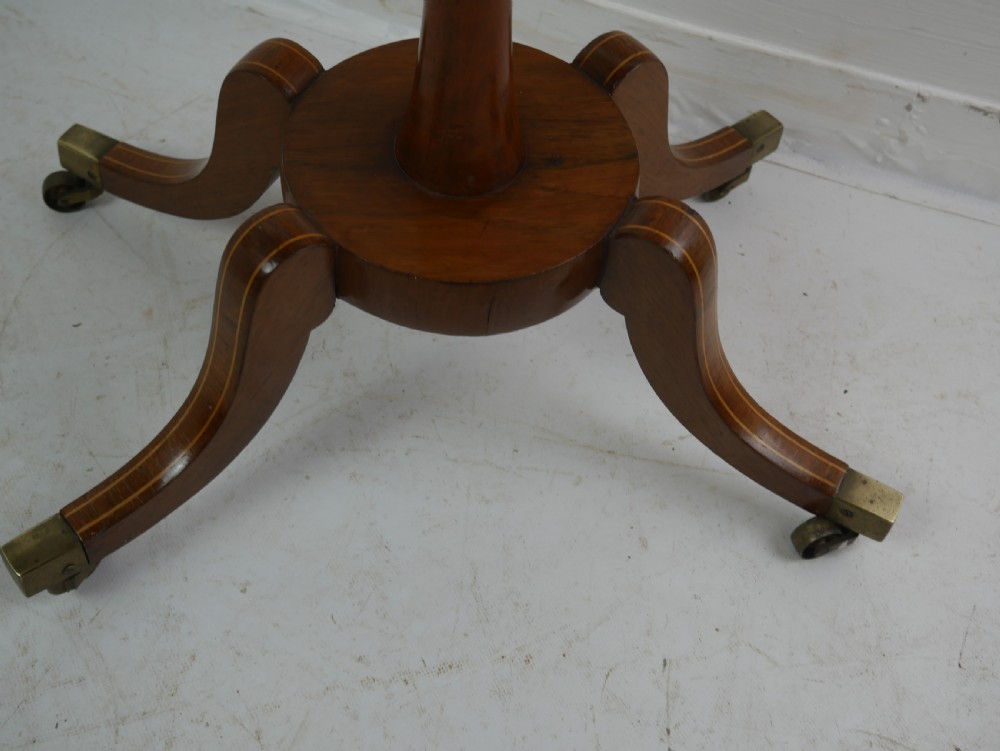 A Regency mahogany sewing table featuring a rectangular top with string inlay, a pleated red fabric work bin below, a turned pedestal support, and four splayed legs with brass castors. View V