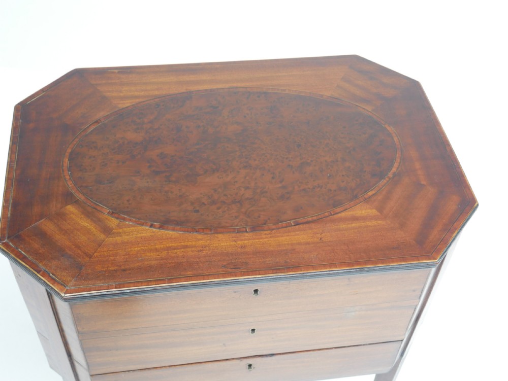 A Sheraton period mahogany occasional table featuring three stacked drawers, canted corners, splayed legs with brass castors, and an X-stretcher. View II
