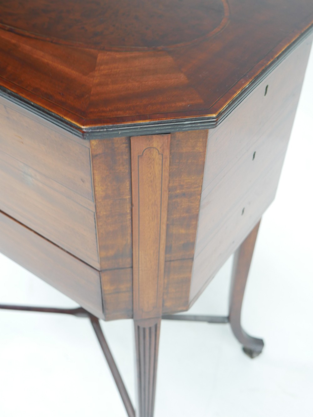 A Sheraton period mahogany occasional table featuring three stacked drawers, canted corners, splayed legs with brass castors, and an X-stretcher. View VII