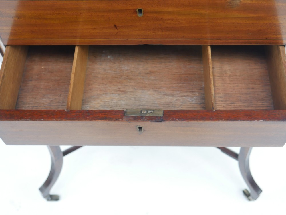 A Sheraton period mahogany occasional table featuring three stacked drawers, canted corners, splayed legs with brass castors, and an X-stretcher. View IX