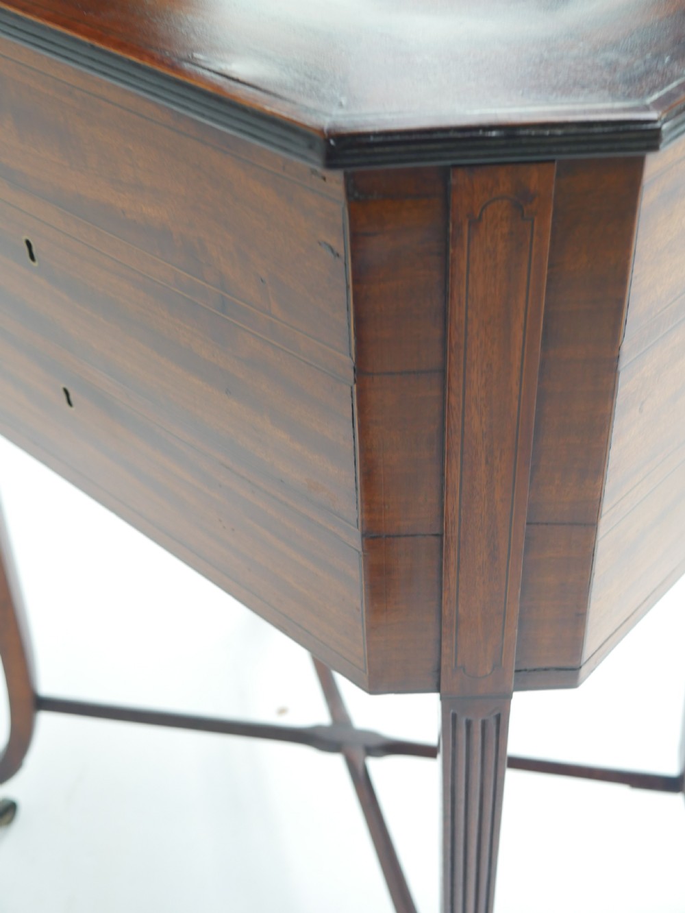 A Sheraton period mahogany occasional table featuring three stacked drawers, canted corners, splayed legs with brass castors, and an X-stretcher. View XI