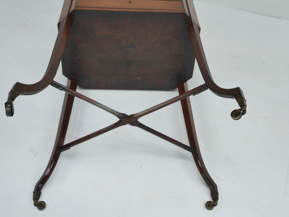 A Sheraton period mahogany occasional table featuring three stacked drawers, canted corners, splayed legs with brass castors, and an X-stretcher. View XIII
