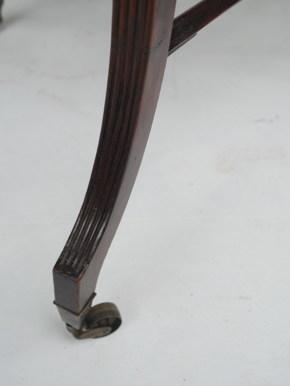 A Sheraton period mahogany occasional table featuring three stacked drawers, canted corners, splayed legs with brass castors, and an X-stretcher. View III