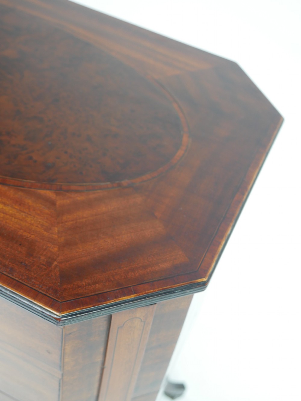 A Sheraton period mahogany occasional table featuring three stacked drawers, canted corners, splayed legs with brass castors, and an X-stretcher. View V
