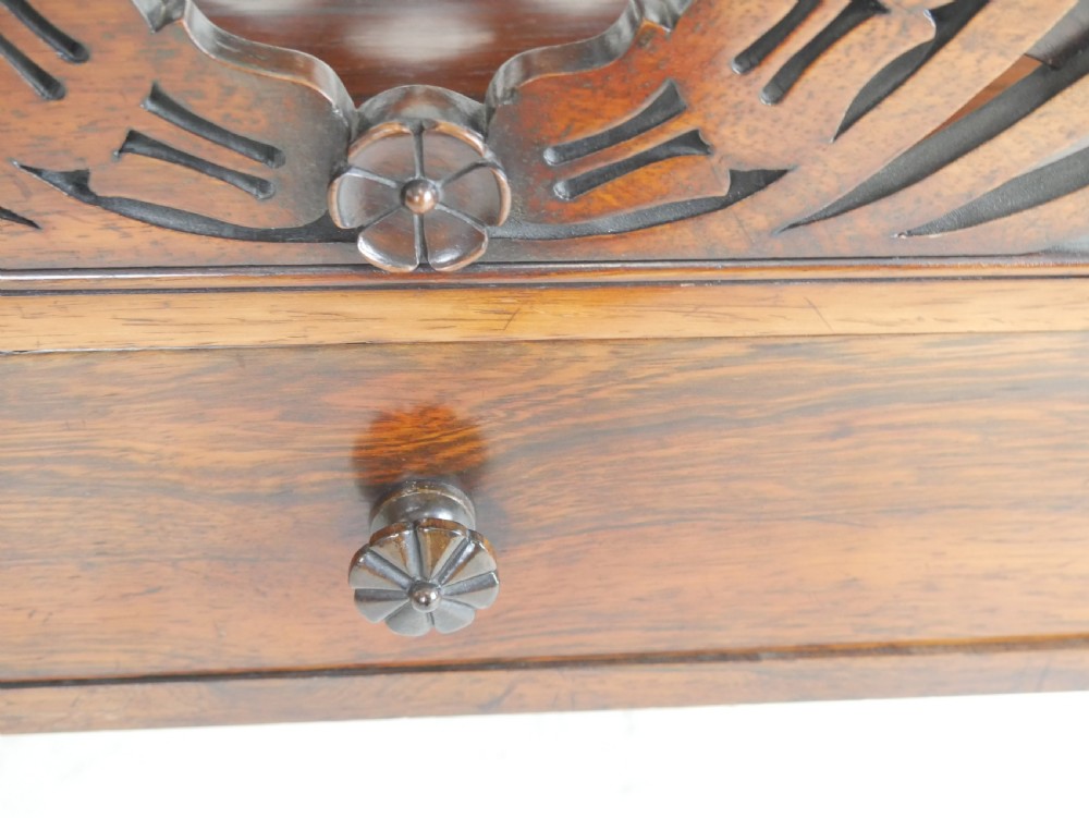 A Regency period dark rosewood music canterbury featuring a carved central wreath handle, slatted divided compartments, a single base drawer, and turned legs on brass castors. View III