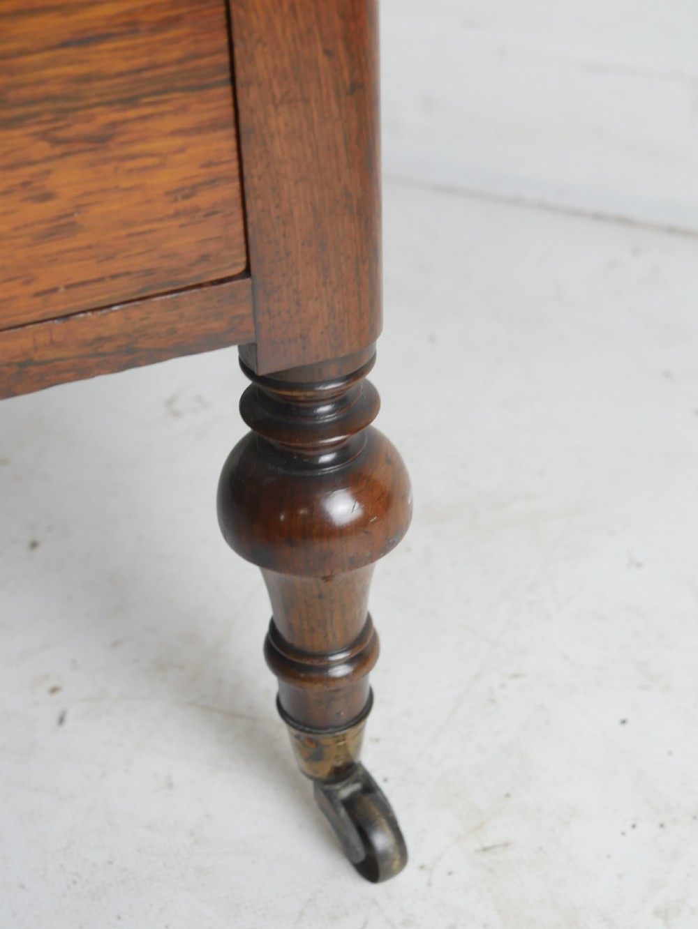 A Regency period dark rosewood music canterbury featuring a carved central wreath handle, slatted divided compartments, a single base drawer, and turned legs on brass castors. View VI