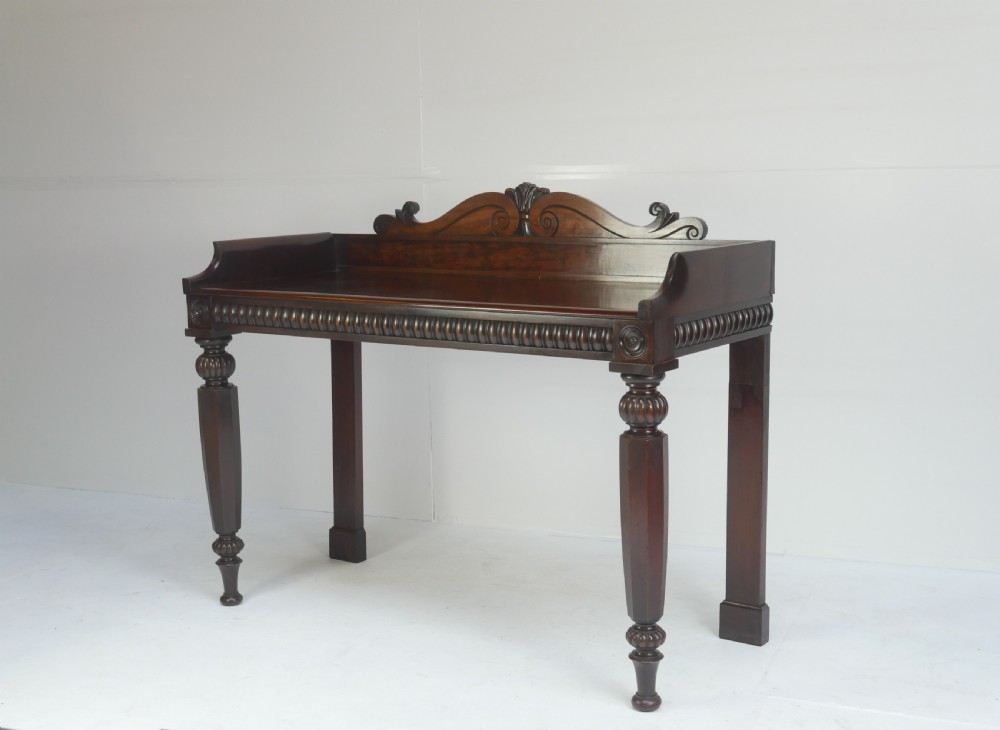 A dark mahogany Regency console table featuring a carved scrollwork gallery back, a reeded apron, and turned front legs.