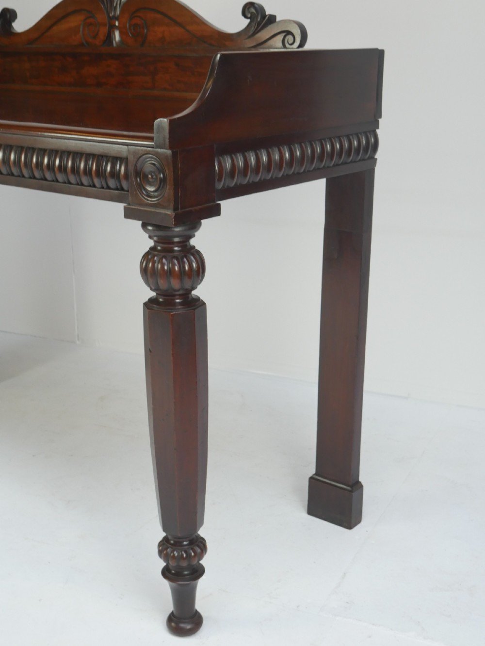 A dark mahogany Regency console table featuring a carved scrollwork gallery back, a reeded apron, and turned front legs. View V