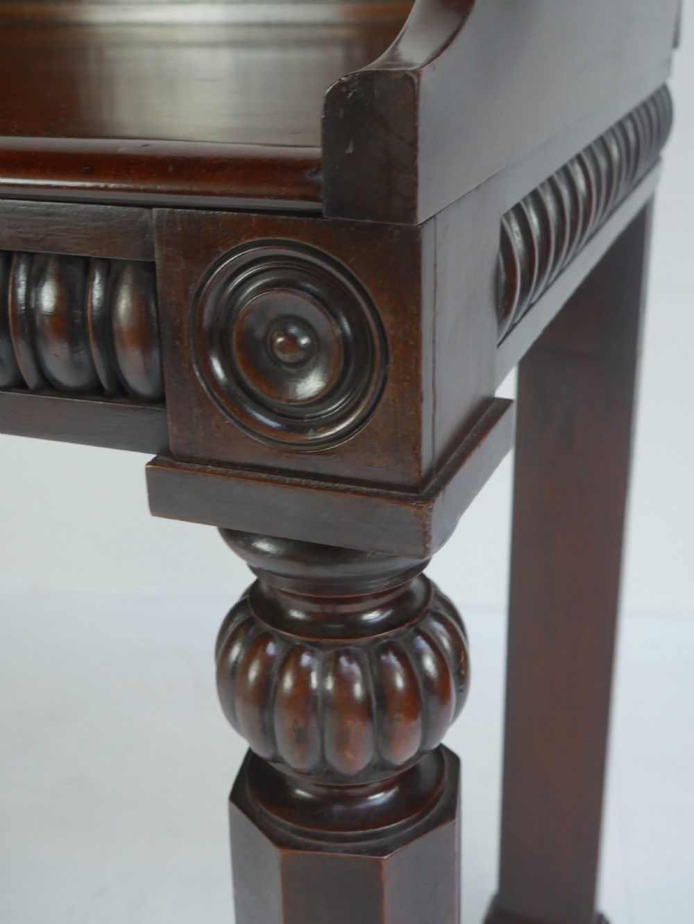 A dark mahogany Regency console table featuring a carved scrollwork gallery back, a reeded apron, and turned front legs. View VI