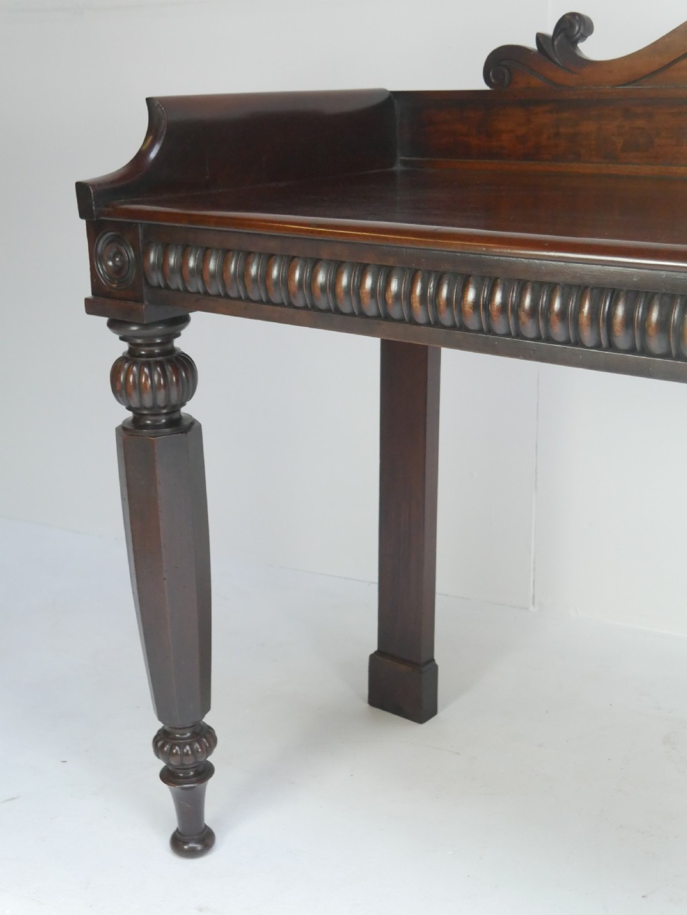 A dark mahogany Regency console table featuring a carved scrollwork gallery back, a reeded apron, and turned front legs. View VII