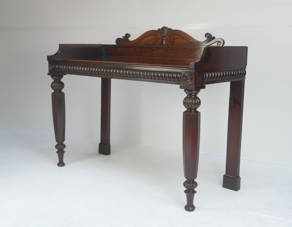 A dark mahogany Regency console table featuring a carved scrollwork gallery back, a reeded apron, and turned front legs. View XI