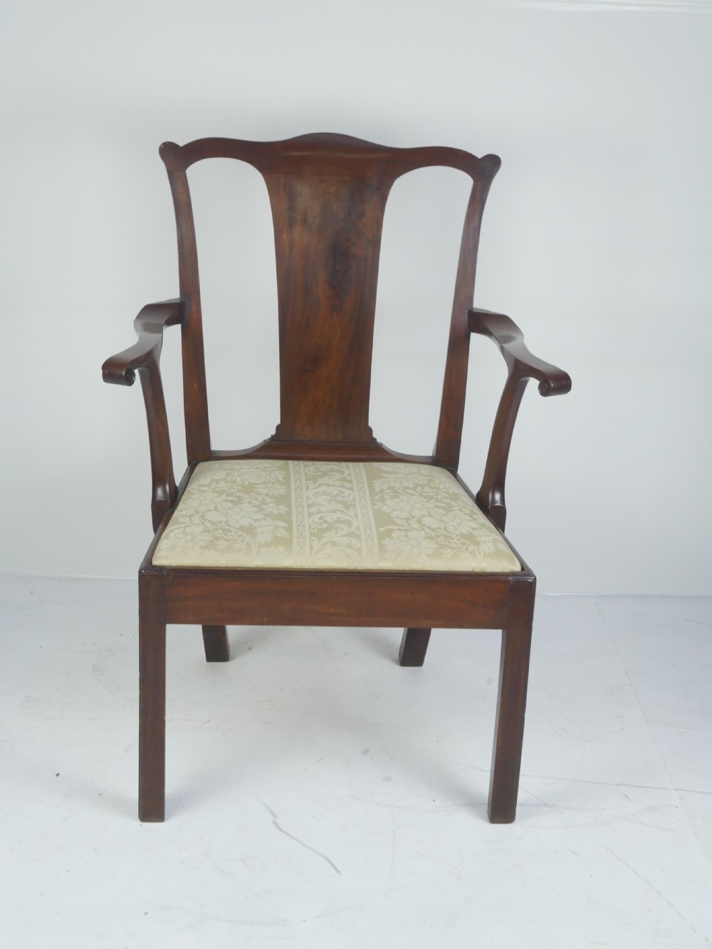 A Georgian mahogany open armchair featuring a vase-shaped splat back, curved armrests, and a cream pattern upholstered seat.