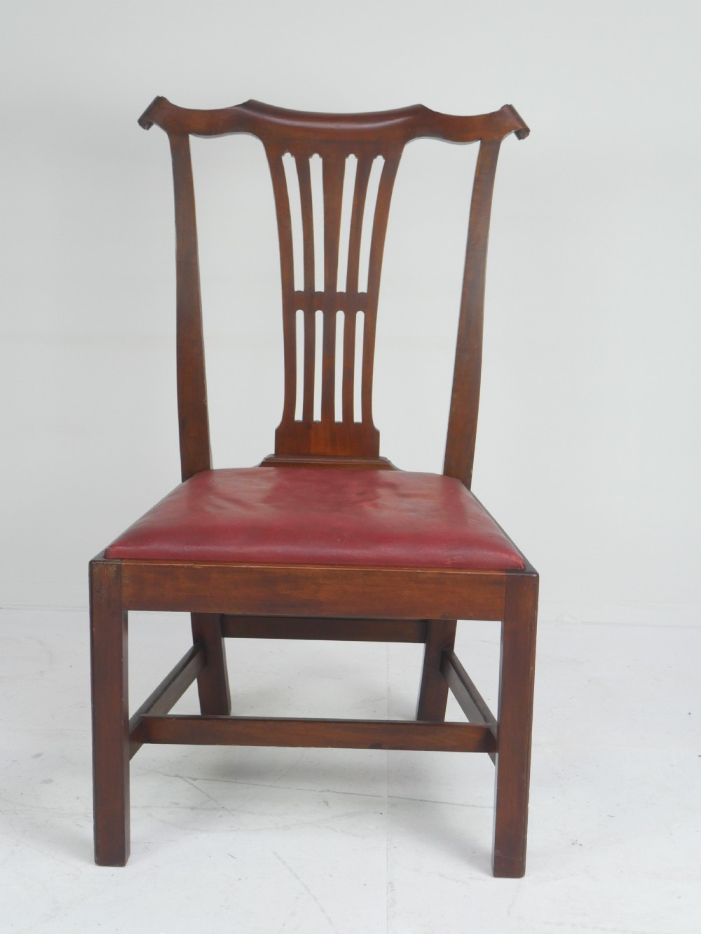 A pair of 19th-century mahogany side chairs with pierced back splats, serpentine top rails, straight legs with stretchers, and red leather seats. View V