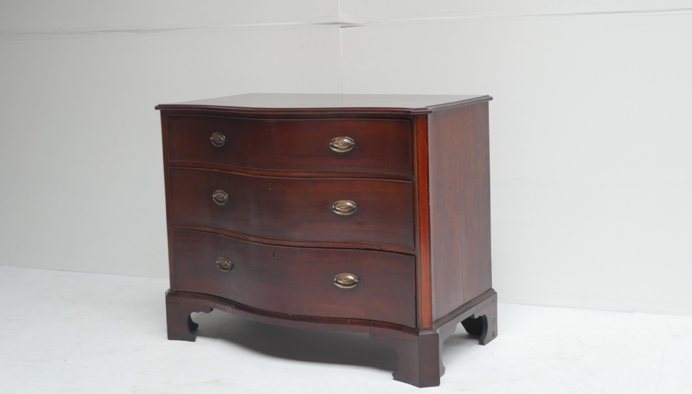 A Georgian dark mahogany chest of drawers with a serpentine curved front, three long drawers fitted with brass oval handles, standing on bracket feet.
