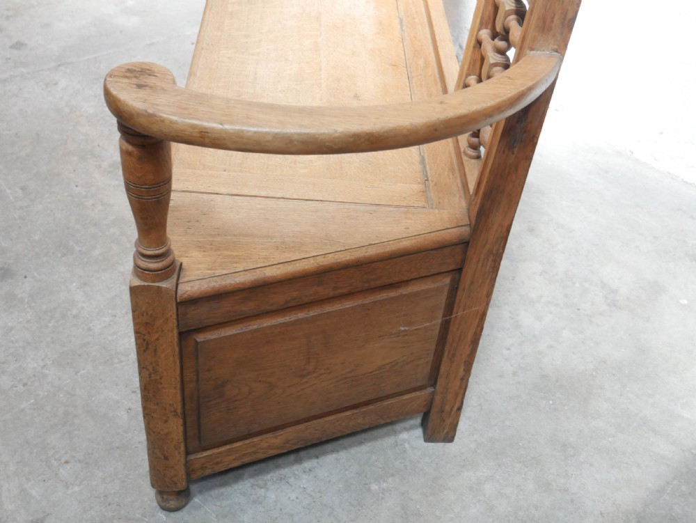 An antique light oak hall settle featuring a turned spindle lattice backrest, sweeping curved armrests, and a lift-up storage seat box. View III
