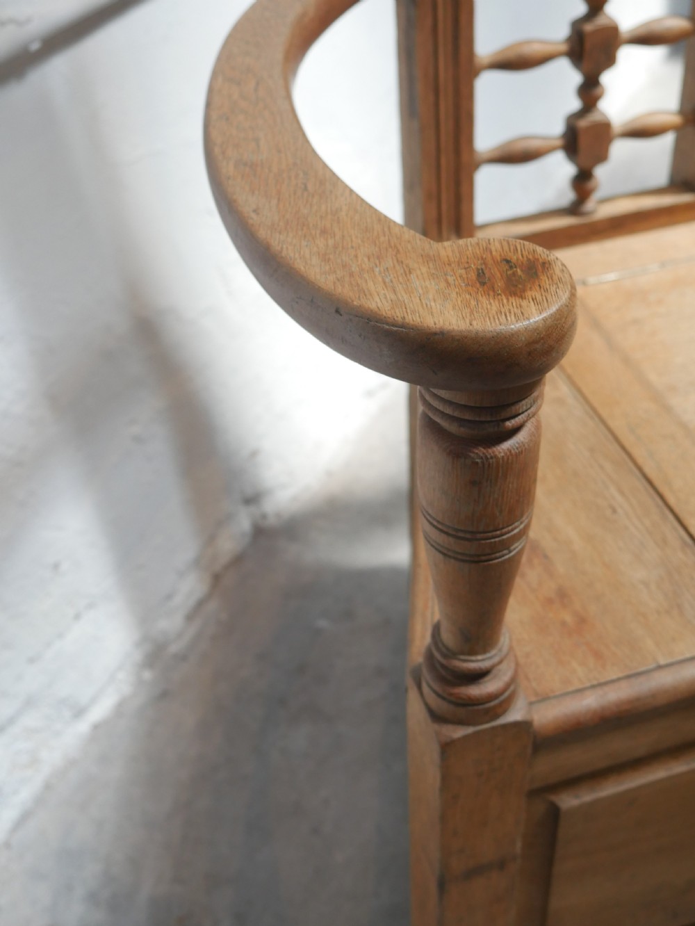An antique light oak hall settle featuring a turned spindle lattice backrest, sweeping curved armrests, and a lift-up storage seat box. View VII