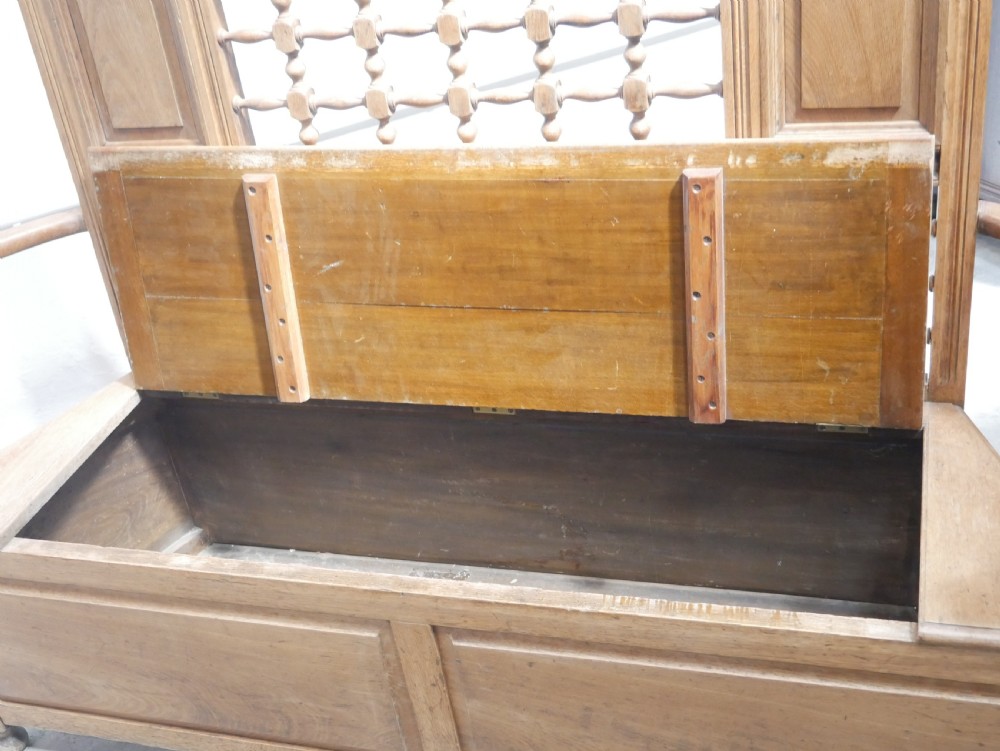 An antique light oak hall settle featuring a turned spindle lattice backrest, sweeping curved armrests, and a lift-up storage seat box. View VIII