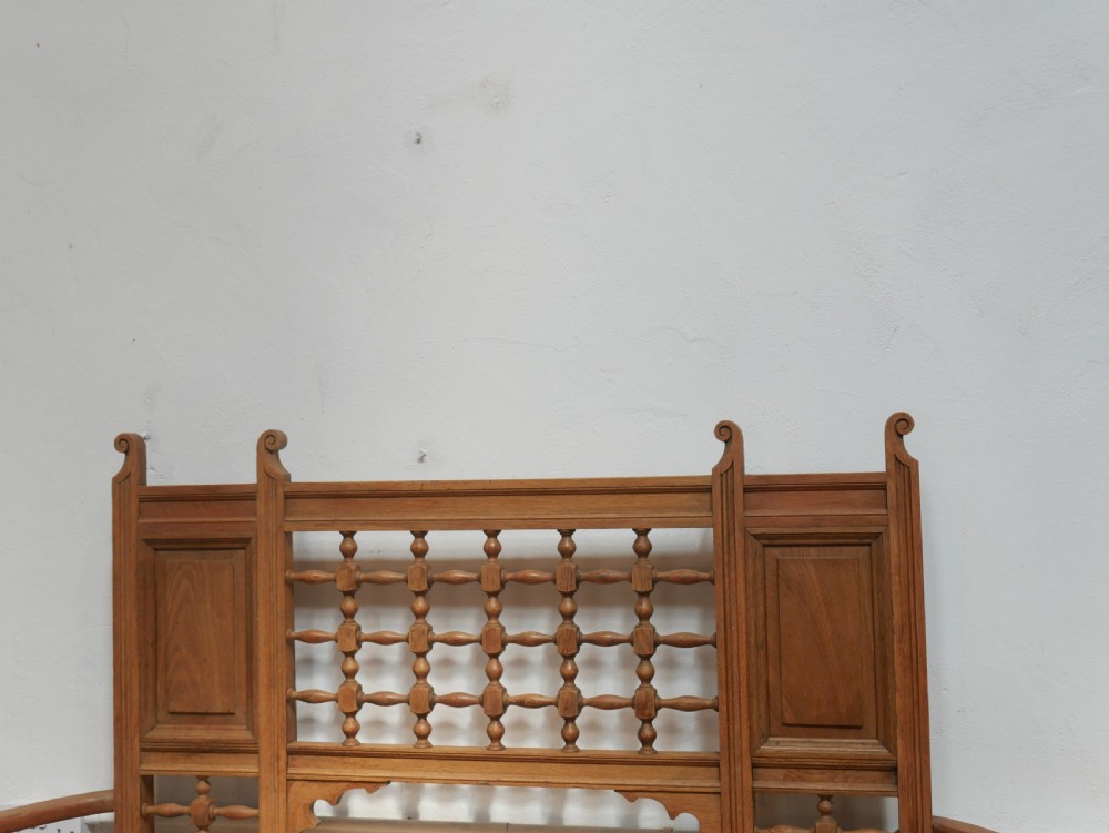 An antique light oak hall settle featuring a turned spindle lattice backrest, sweeping curved armrests, and a lift-up storage seat box. View XIII