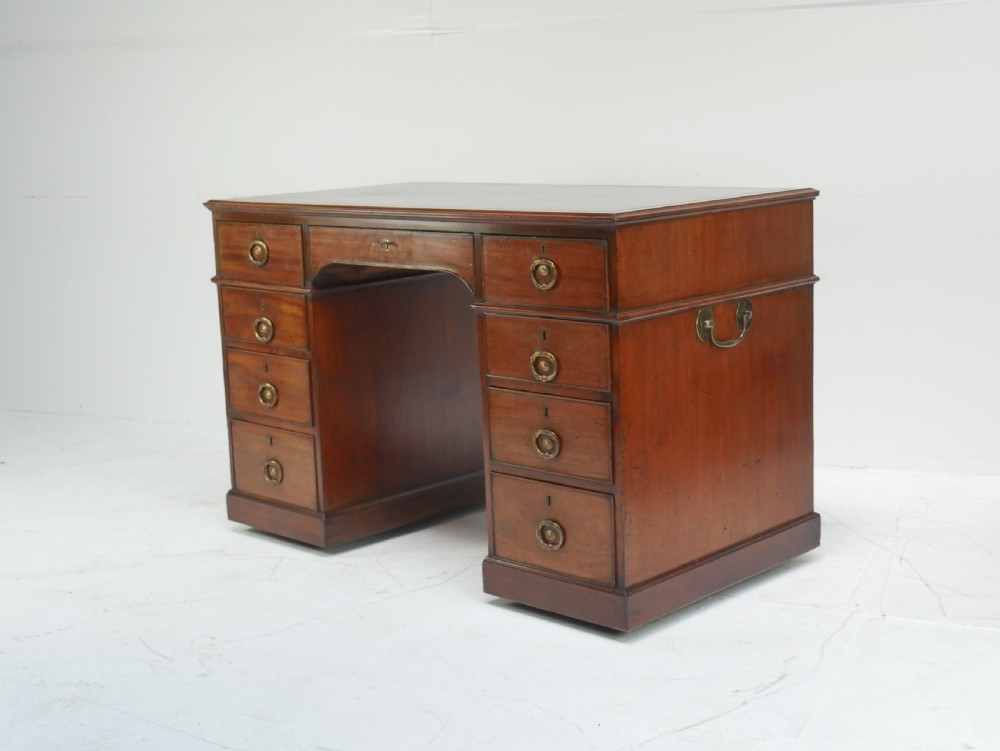 A Georgian mahogany kneehole desk featuring multiple side drawers with brass ring handles and a plinth base.
