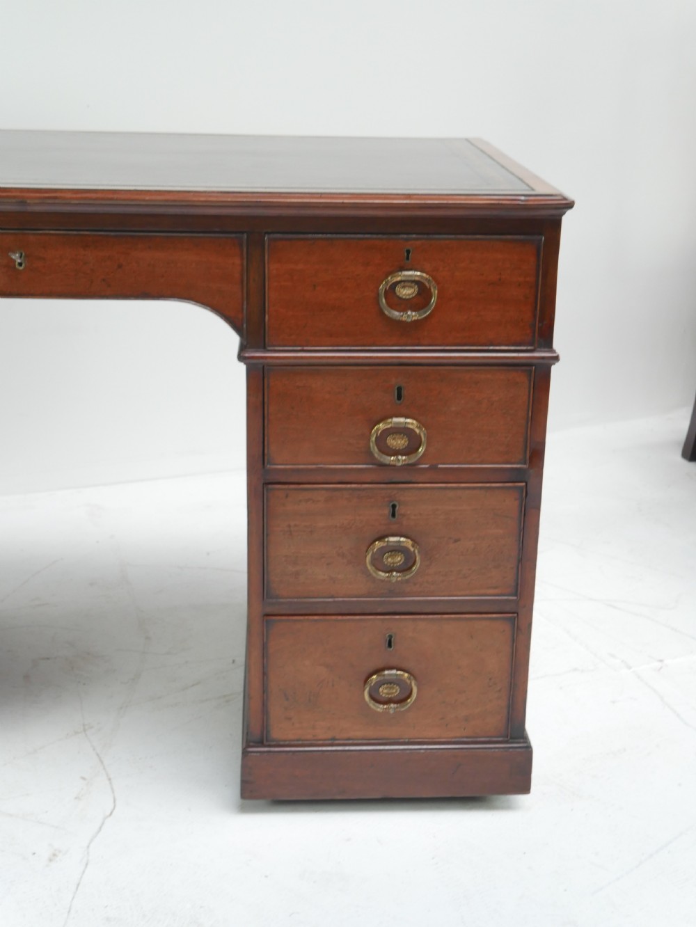 A Georgian mahogany kneehole desk featuring multiple side drawers with brass ring handles and a plinth base. View X