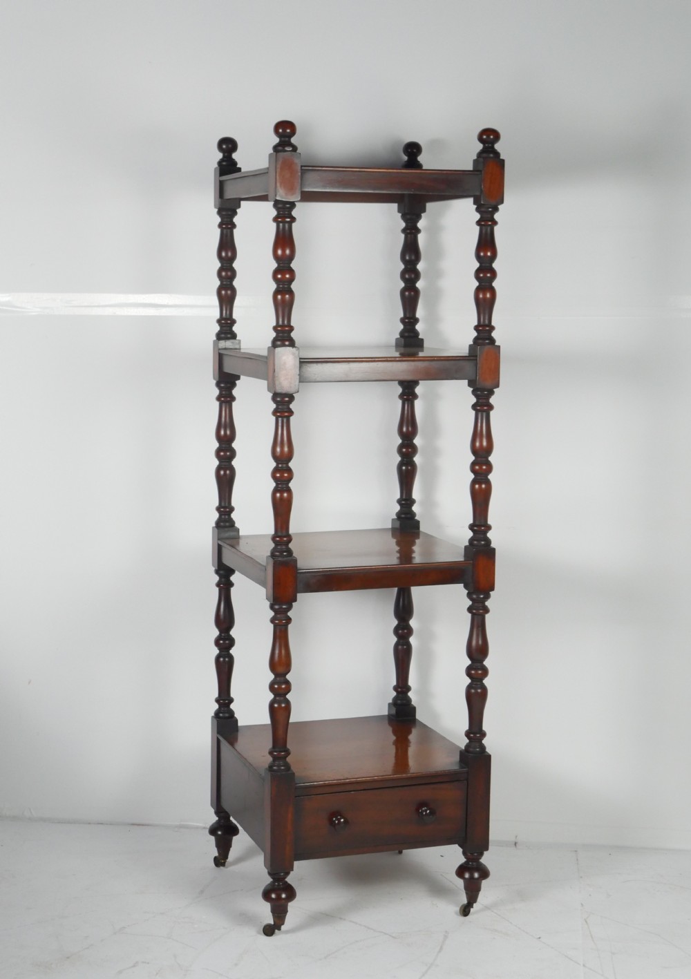 A tall Victorian mahogany four-tier whatnot featuring turned spindle supports, finials, a lower drawer with twin knobs, and castor feet.