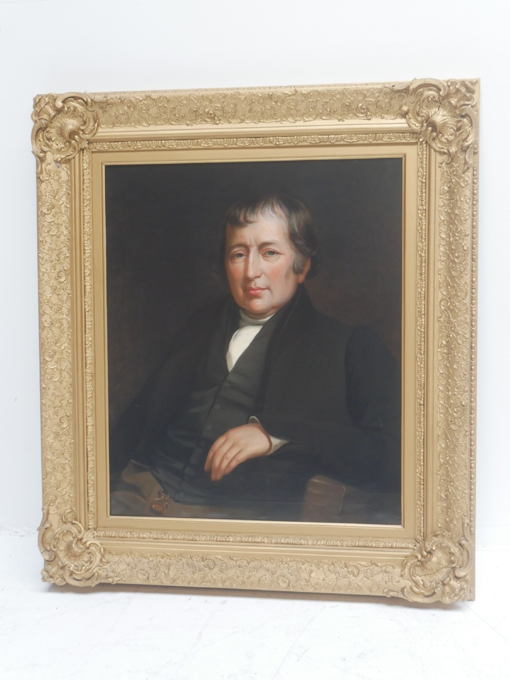 A 19th-century oil painting depicting a gentleman in formal dark attire, framed within an elaborate gold gilt frame. View IX