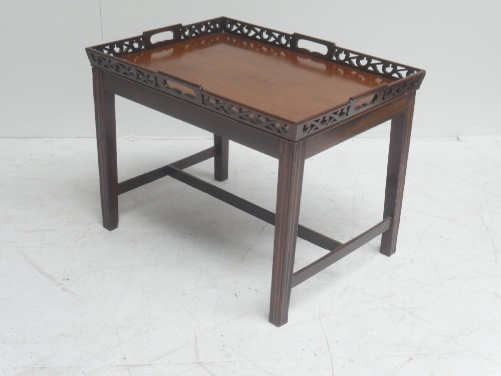 An early 20th-century dark mahogany butler tray table with a pierced fretwork gallery rim mounted on a four-legged wooden stand.
