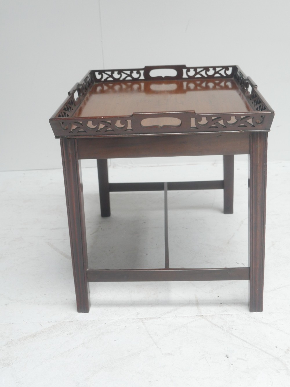 An early 20th-century dark mahogany butler tray table with a pierced fretwork gallery rim mounted on a four-legged wooden stand. View II