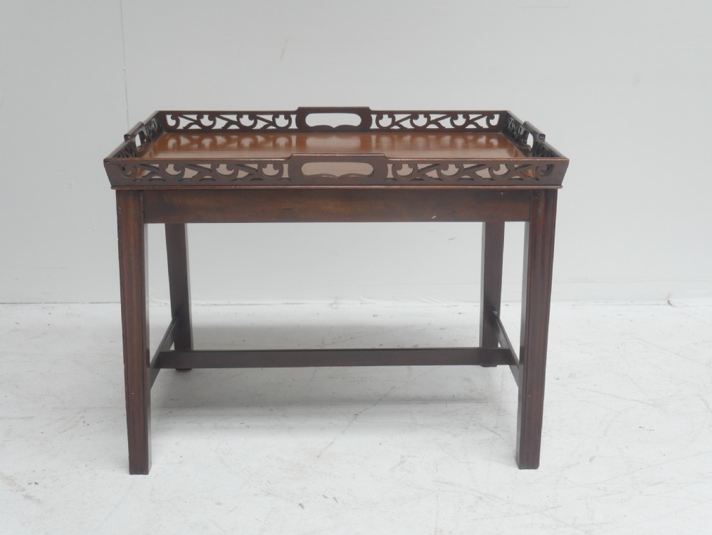An early 20th-century dark mahogany butler tray table with a pierced fretwork gallery rim mounted on a four-legged wooden stand. View VII