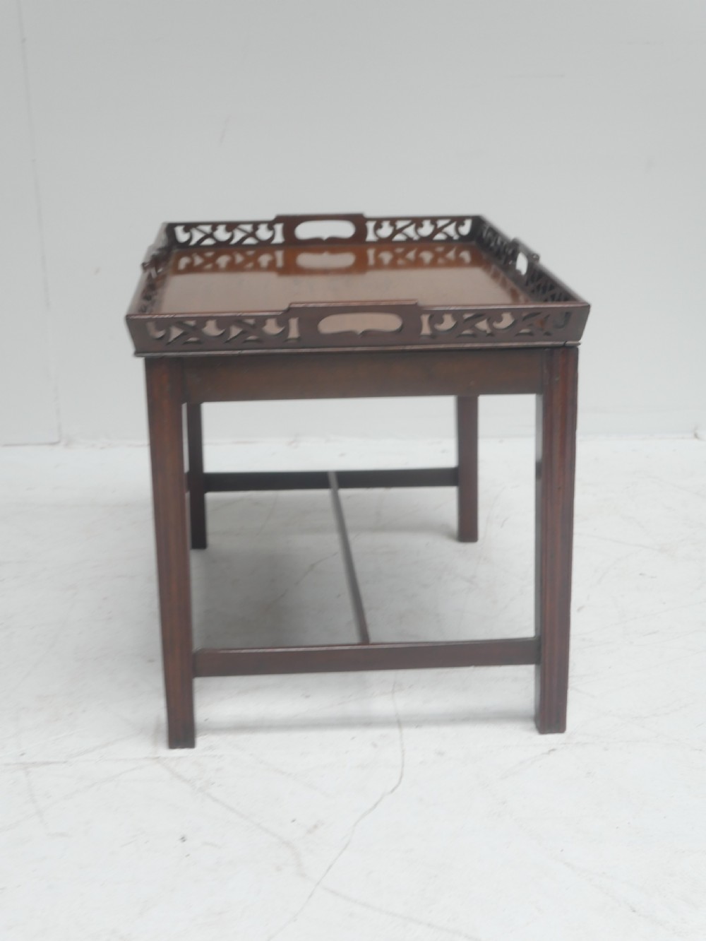An early 20th-century dark mahogany butler tray table with a pierced fretwork gallery rim mounted on a four-legged wooden stand. View VIII