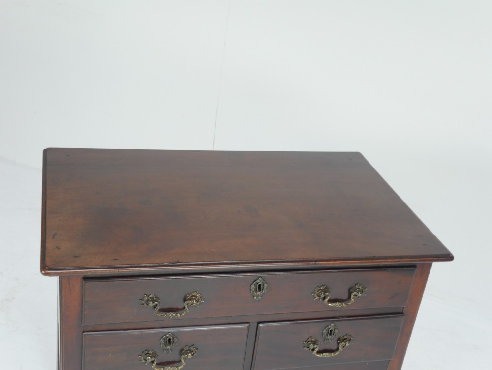 A dark brown Georgian mahogany lowboy featuring three drawers with brass handles and a shaped lower apron on square legs. View II