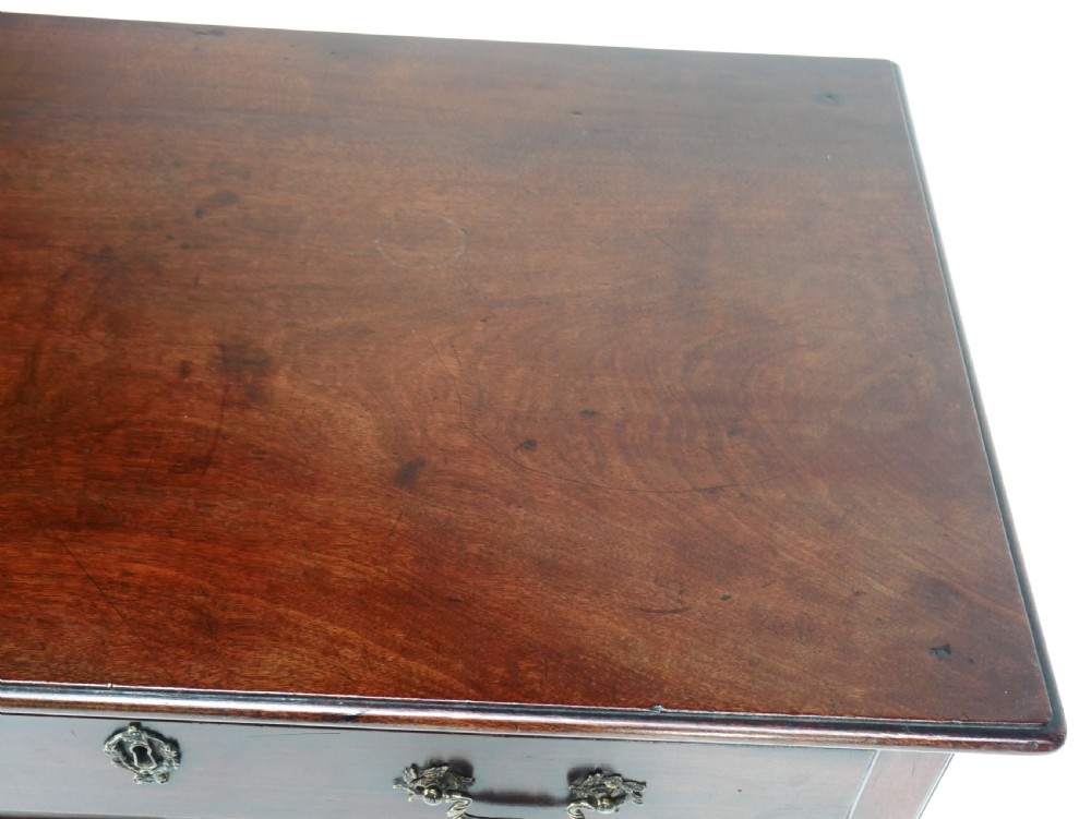 A dark brown Georgian mahogany lowboy featuring three drawers with brass handles and a shaped lower apron on square legs. View III