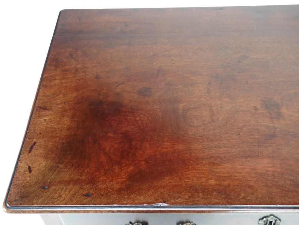 A dark brown Georgian mahogany lowboy featuring three drawers with brass handles and a shaped lower apron on square legs. View V