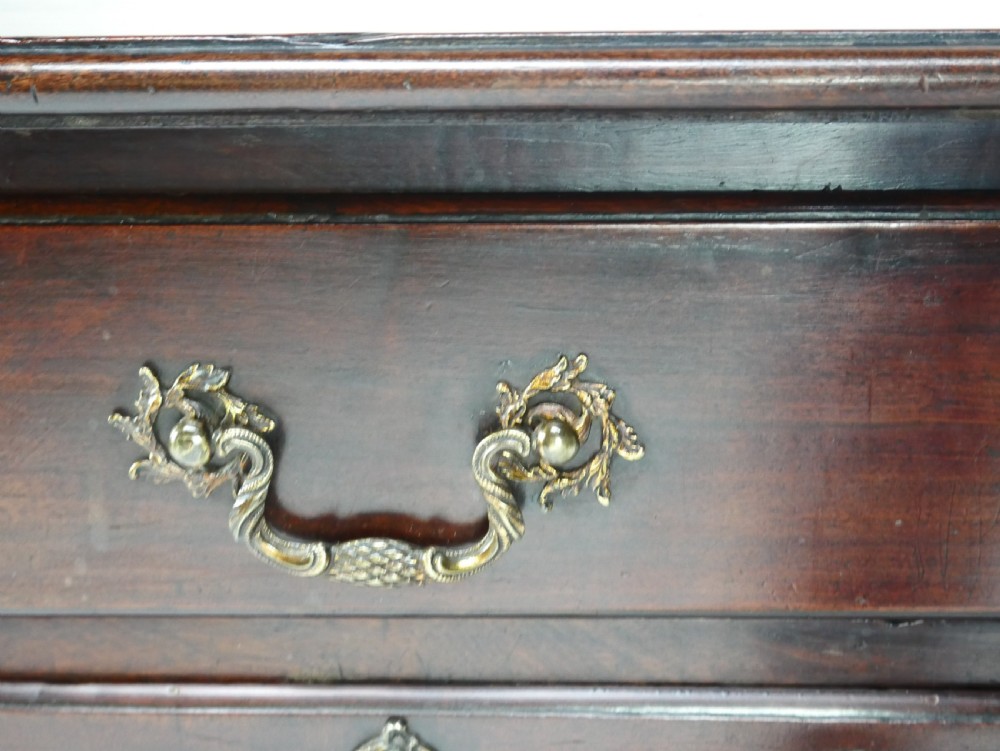 A dark brown Georgian mahogany lowboy featuring three drawers with brass handles and a shaped lower apron on square legs. View VI