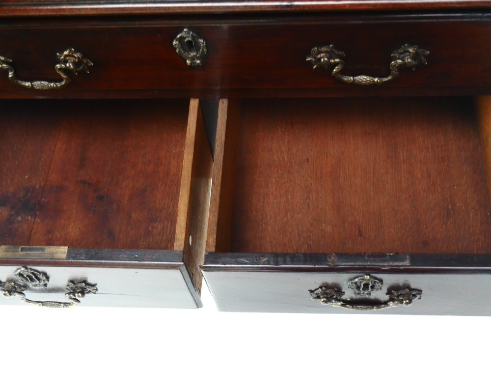 A dark brown Georgian mahogany lowboy featuring three drawers with brass handles and a shaped lower apron on square legs. View VII