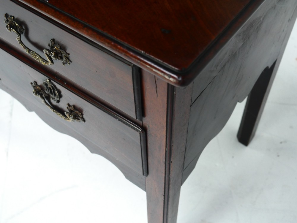 A dark brown Georgian mahogany lowboy featuring three drawers with brass handles and a shaped lower apron on square legs. View X
