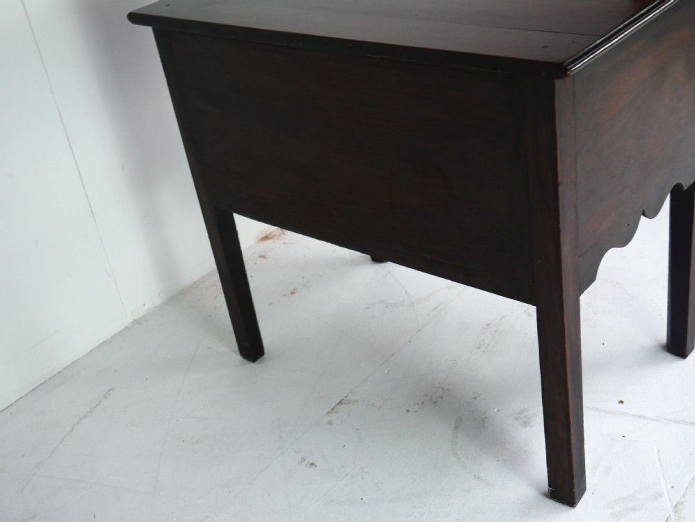 A dark brown Georgian mahogany lowboy featuring three drawers with brass handles and a shaped lower apron on square legs. View XII