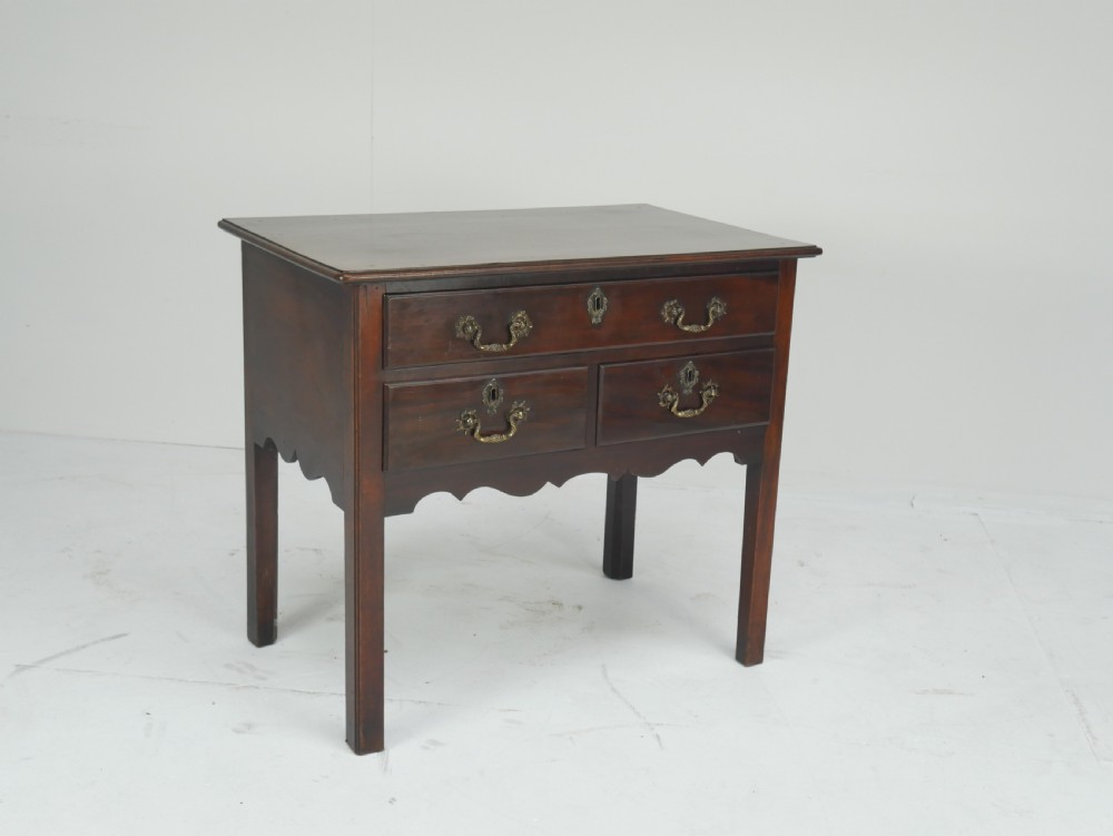 A dark brown Georgian mahogany lowboy featuring three drawers with brass handles and a shaped lower apron on square legs. View XIV