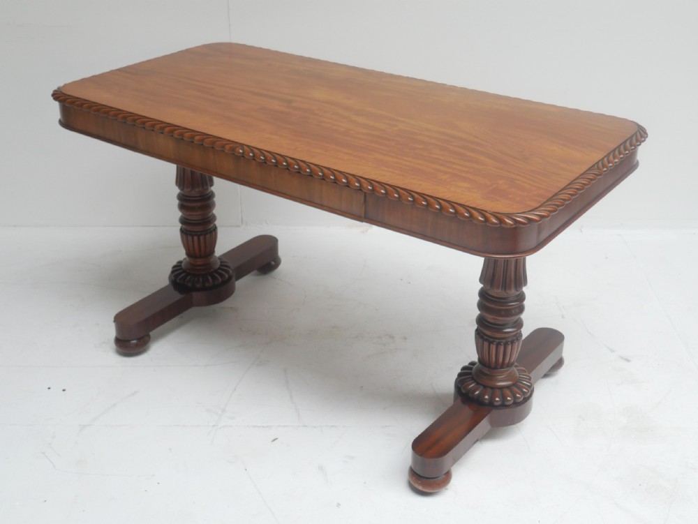 A Regency mahogany sofa writing table featuring a carved gadrooned edge, twin turned pedestal supports, and plinth feet.
