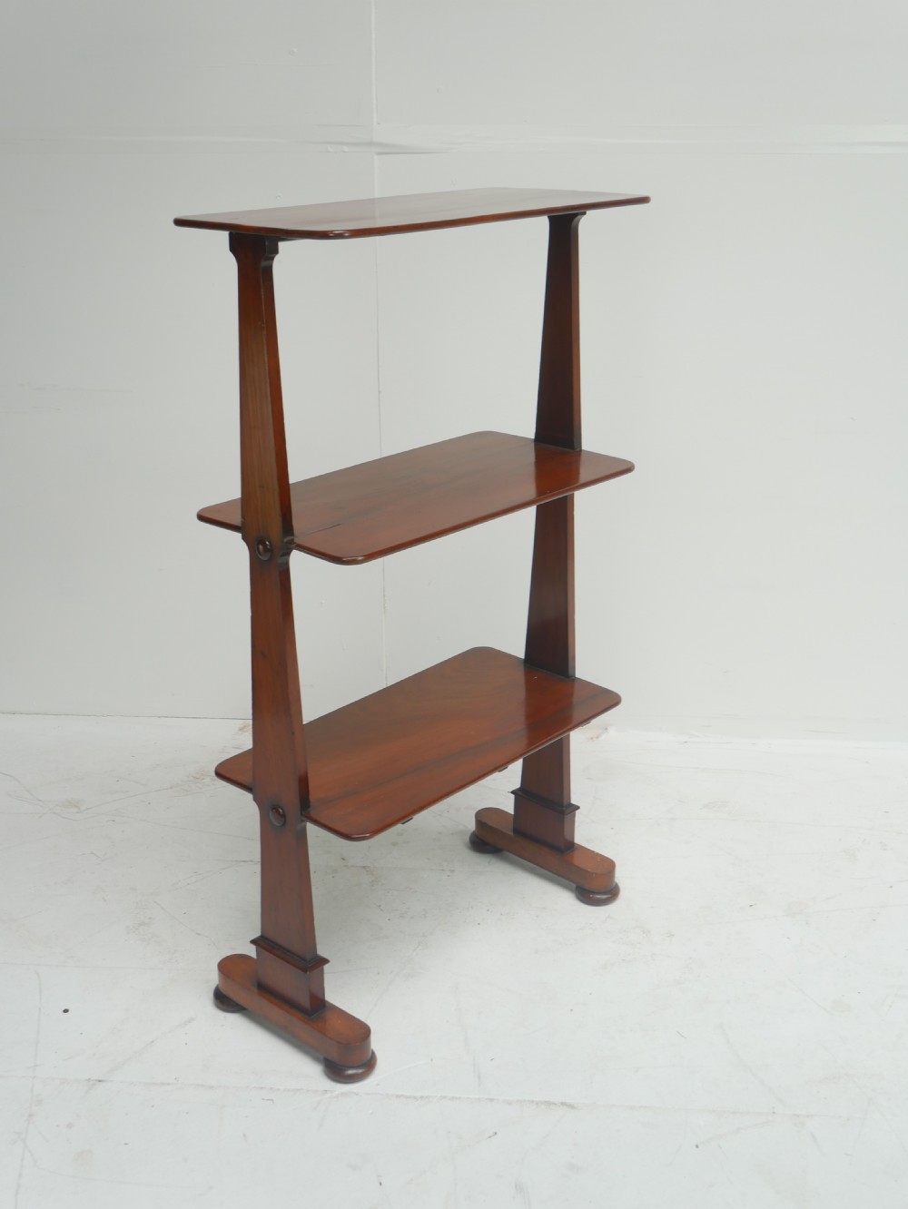 A 19th-century warm brown mahogany whatnot shelf unit featuring three open rectangular tiers supported by tapered upright side panels resting on trestle feet.